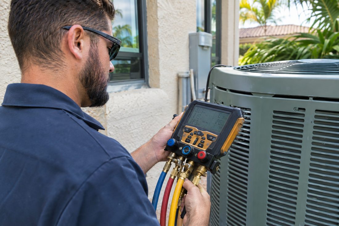 A technician checking refrigerant pressures with digital manifold gauges at a Spanish-style stucco home in West Palm Beach, FL